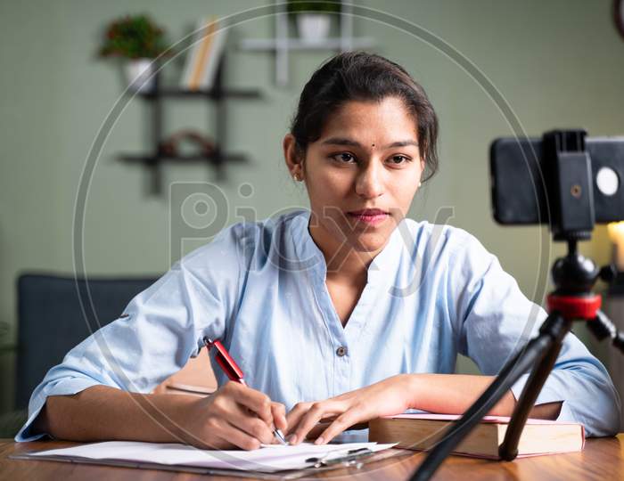 Young College Girl Student Writing Notes By Looking Into Mobile Phone During Online Class - Concept Of New Normal, Virtual Learning, Online Education During Coronavirus Or Covid-19 Pandemic.