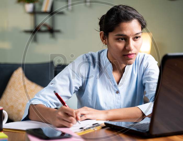 Young Business Woman Writing Down Notes By Looking Laptop - Concept Of Employee Or Student Online Training Class At Home.