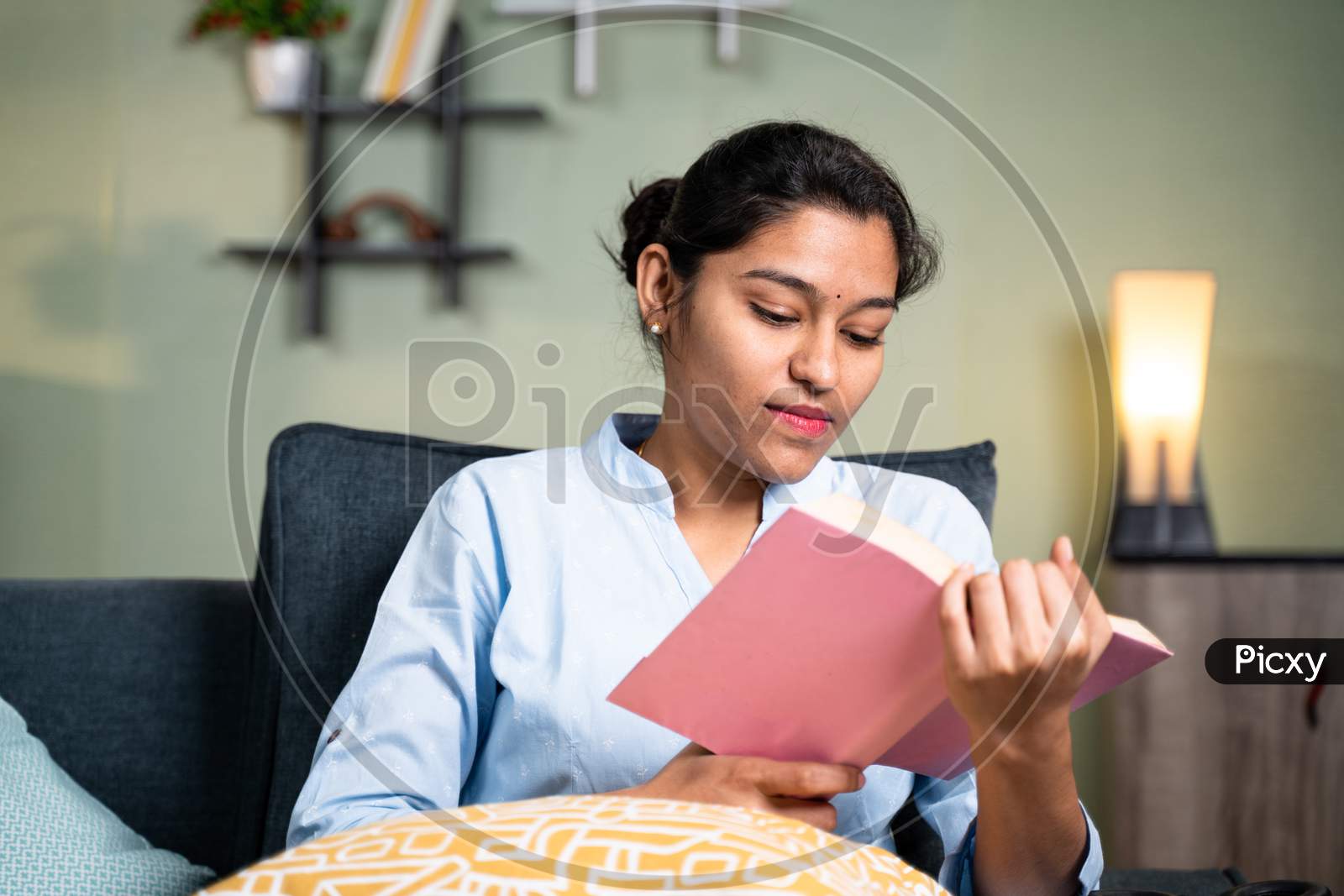 Concentrated Young Girl Reading Book Or Studying During Leisure Time Or For Examination At Home By Sitting On Sofa - Concept Of Reading Hobby.