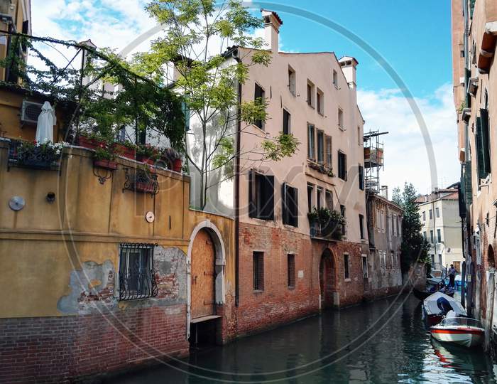 Venice, Italy - September 03, 2018: Wide Angle Shot Of Rusty Italian Architecture On River Canal With Gandola Boats Against Clear Blue Sky