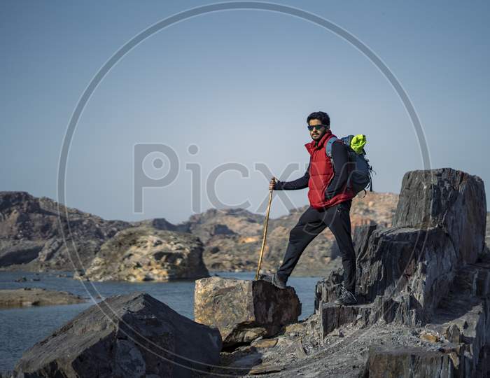 Young Indian Traveler Standing Confidently On Top Of The Mountain Over A Cliff, Wearing A Red Snow Jacket. Confident And Success Concept.