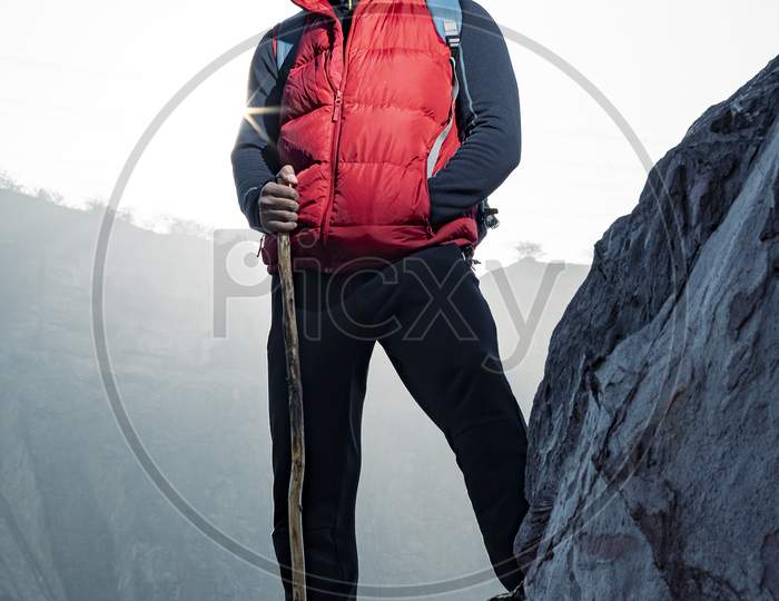 Young Indian Traveler Standing Confidently On Top Of The Mountain Over A Cliff, Wearing A Red Snow Jacket. Confident And Success Concept.