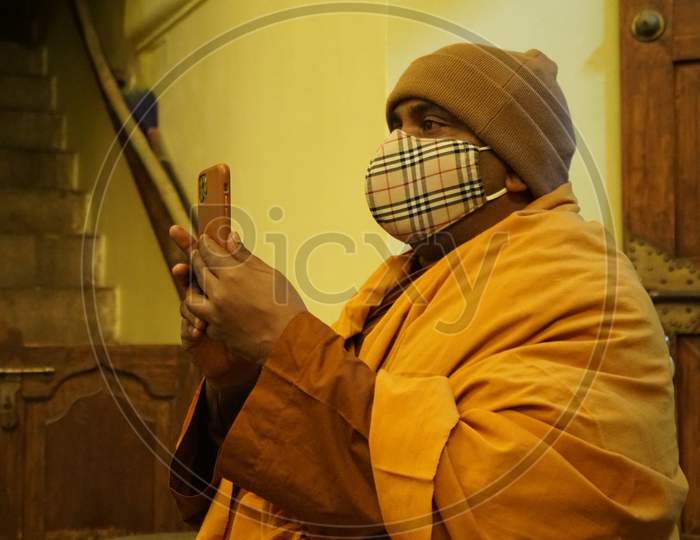Buddhist Monk wearing a designer mask takes a photo on his smartphone