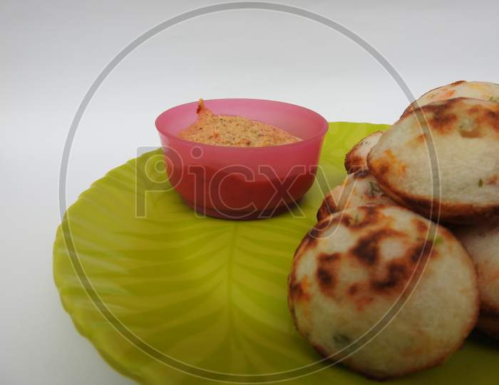 Paddu or Kuzhi paniyaram and Coconut Chutney in a Green Plate isolated on White Background. Indian dish made by steaming batter using a mould. The batter is made of black lentils and rice.