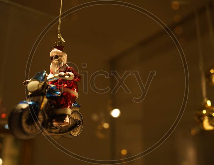 Close-Up Of Santa Clause Bauble On Motorcycle. Retro And Vintage Decoration In Illuminated Showcase In Dark Evening.