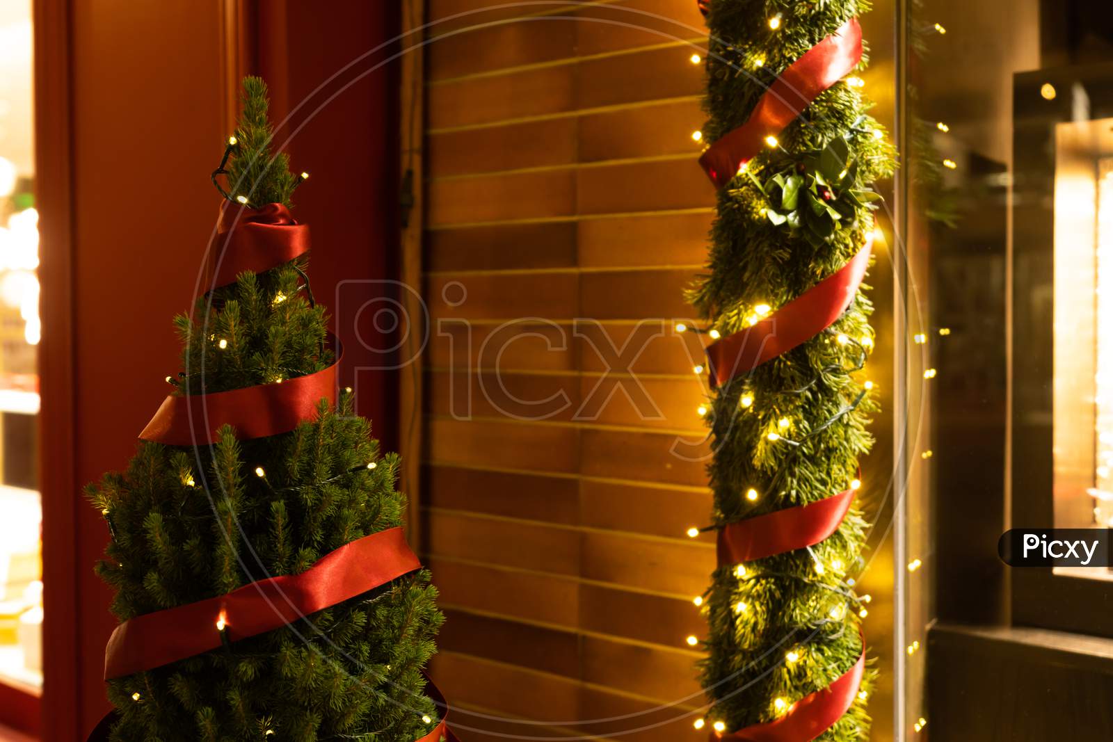 Decorated And Illuminated Store Window With Pine, Red Ribbon, Light And Garland Decoration In Dark Evening.