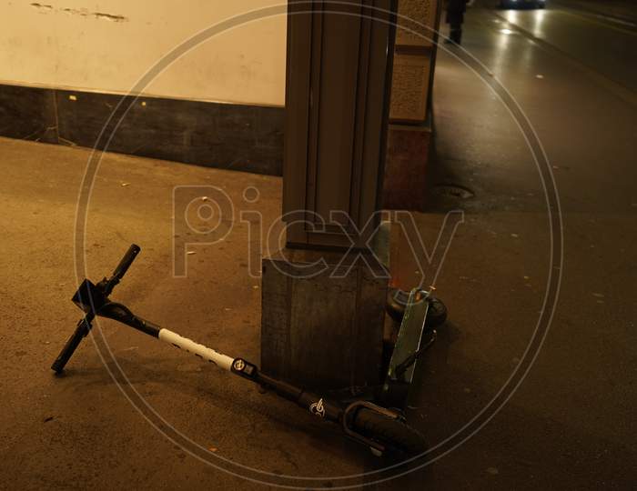Electric Scooter Lying Down On Sidewalk In Dark Evening. Problem Of Share System Rules.