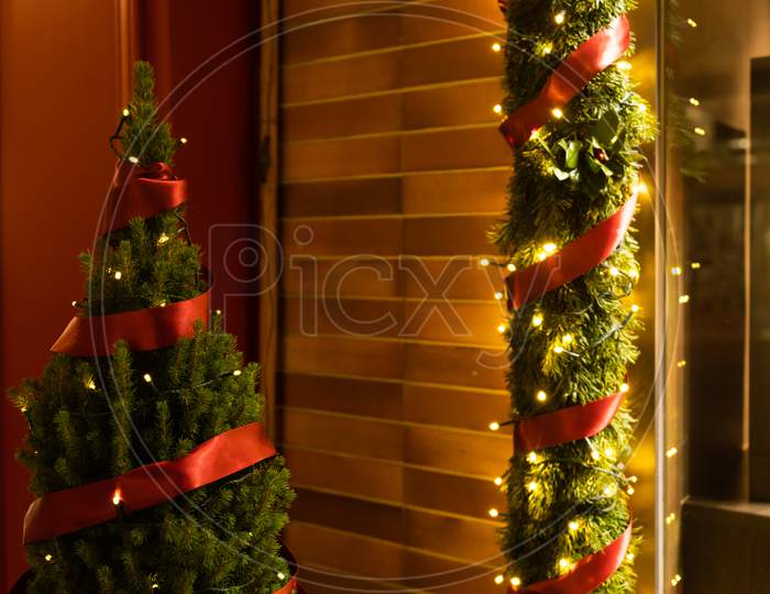 Decorated And Illuminated Store Window With Pine, Red Ribbon, Light And Garland Decoration In Dark Evening.