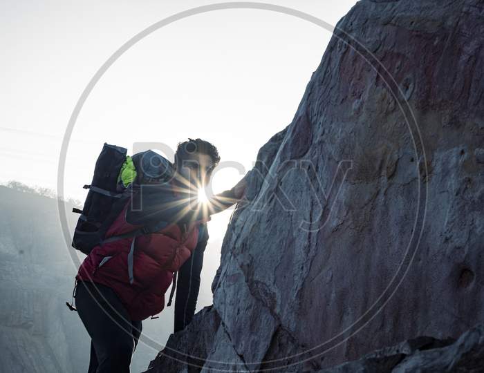 Young Indian Climber And Traveler Climbing Up The Mountain Rock During Sunset. Adventure And Sports Concept.