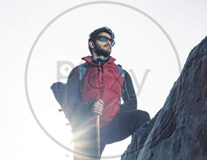 Young Traveler In Red Snow Jacket And A Backpack Standing On Blue Isolated Background. Looking Upwards In The Sky With Confidence . Confidence And Success Concept.