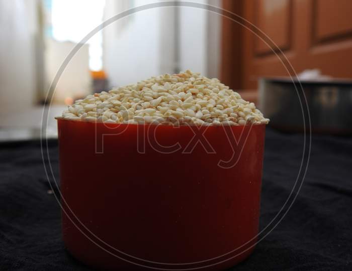 White color Sesame Seeds in a Traditional Sand Bowl and Plastic Cup isolated on black background