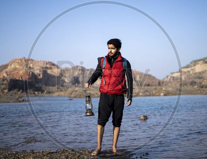 Young Indian Traveler Standing Near A Lake In The Mountains With A Lantern, Getting Ready For Camping In The Night.