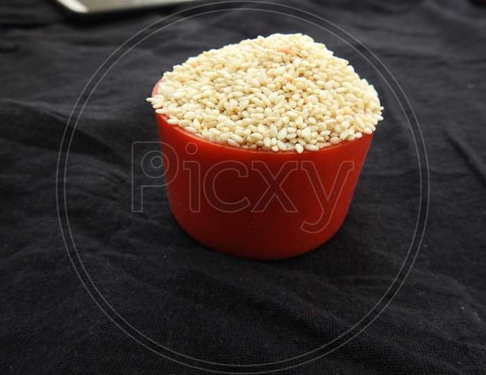 white color Sesame Seeds in a Traditional Sand Bowl and Plastic Cup isolated on black background