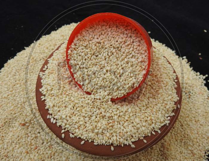 white color Sesame Seeds in a Traditional Sand Bowl and Plastic Cup isolated on black background