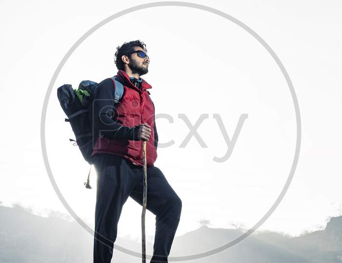 Young Traveler In Red Snow Jacket And A Backpack Standing On Blue Isolated Background. Looking Upwards In The Sky With Confidence . Confidence And Success Concept.