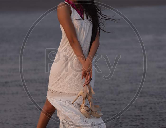 Lifestyle of young Indian woman enjoying her vacation on beach during sun set and wearing white one-piece gown and long flowy sarong