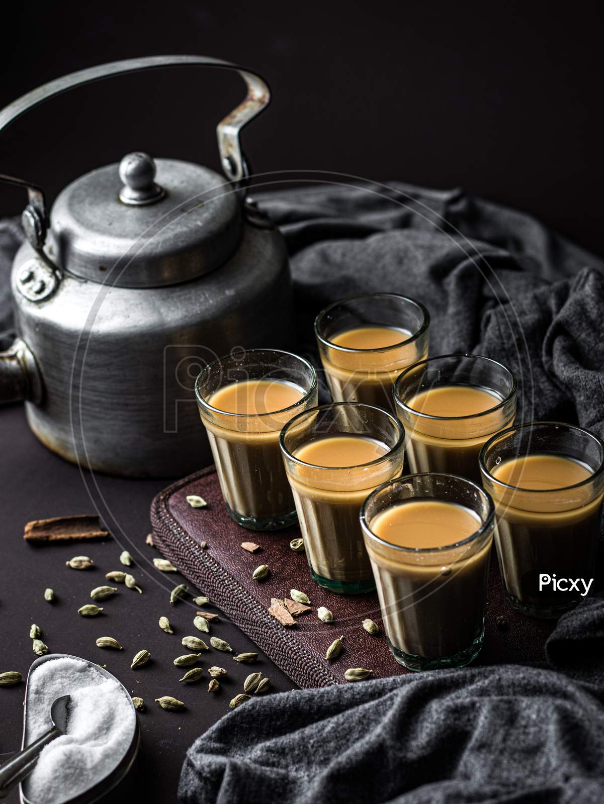 Indian chai in glass cups with metal kettle and other masalas to make the tea.