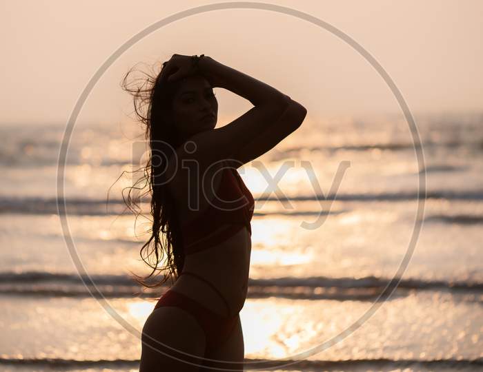 Silhouette of young India girl in red bikini enjoying her vacation on beach and relaxing on beach