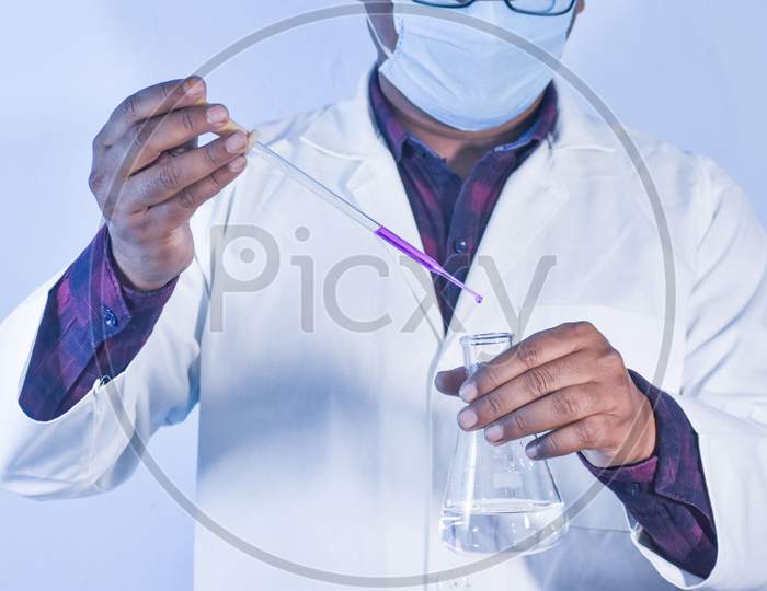 Scientist Pouring Color Liquid Into A Conical Flask With A Dropper In Chemistry Laboratory
