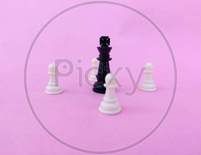 Black Chess Queen Surrounded By White Chess Pawns. Isolated On Pink Background.