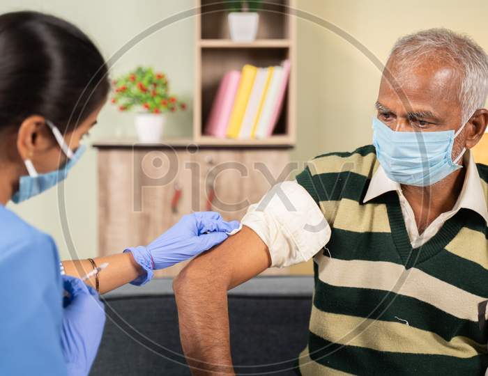 Doctor Preparing Vaccination Shot To Elderly Patient By Holding Syringe At Home - Concept Of Home Health Check To Seniors During Coronavirus Covid-19 Vaccine Immunization.