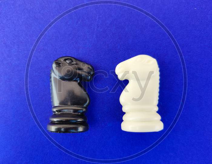 Top View Of Black And White Chess Knight Or Horse Facing Each Other On Blue Background.
