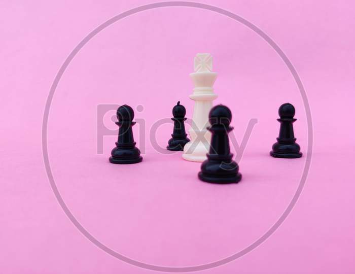 White Chess King Surrounded By Black Chess Pawns. Isolated On Pink Background.