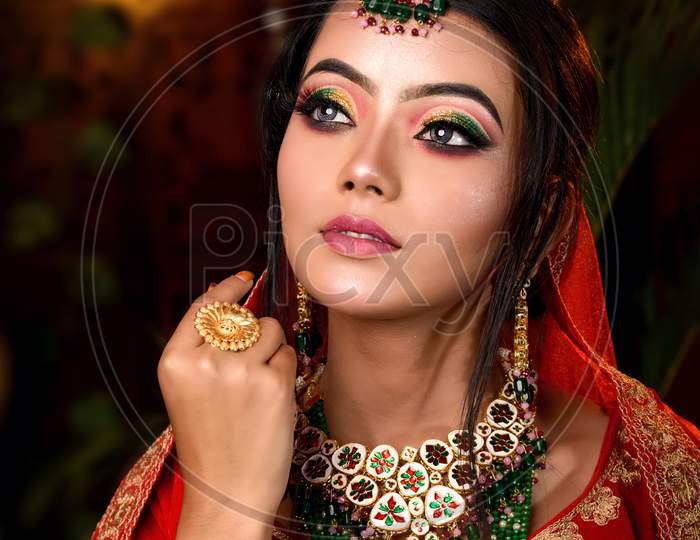 Close Up Portrait Of Very Beautiful Young Indian Bride In Luxurious Bridal Costume With Makeup And Heavy Jewellery In Studio Lighting Indoor. Wedding Fashion.