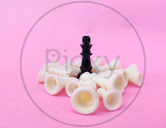 Black Chess King Surrounded By Number Of Fallen White Chess Pieces. Pink Background. Business Concept