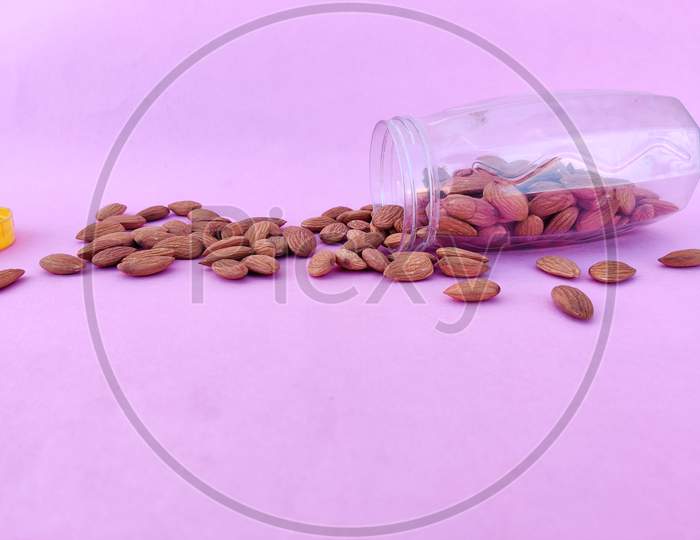 Pile Of Almonds Pour From Plastic Container. Isolated On Pink Background. Healthy