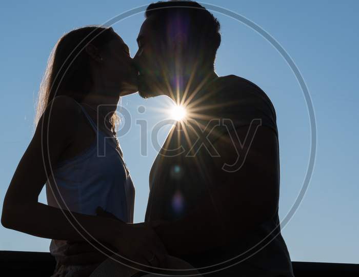 Silhouette Of Kissing Couple Against Deep Blue Sky With Sunbeams. Low Angle View, Concept.