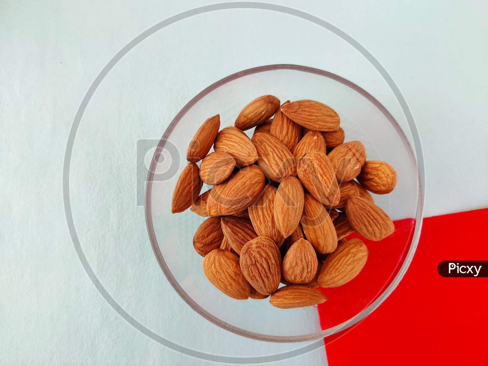 Top View Of Almonds In Glass Bowl On Red And Green Background.