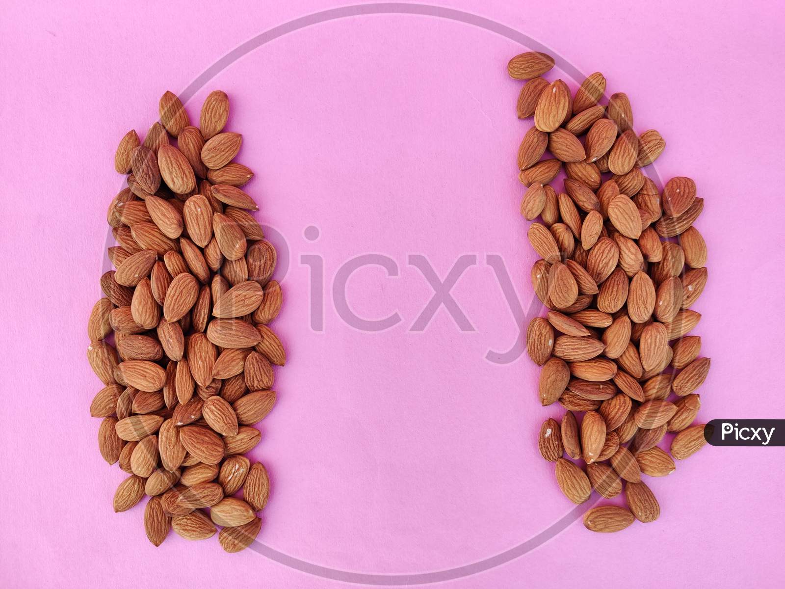 Heap Of Almonds Separated With Copy Space In Center. Isolated On Pink Background.