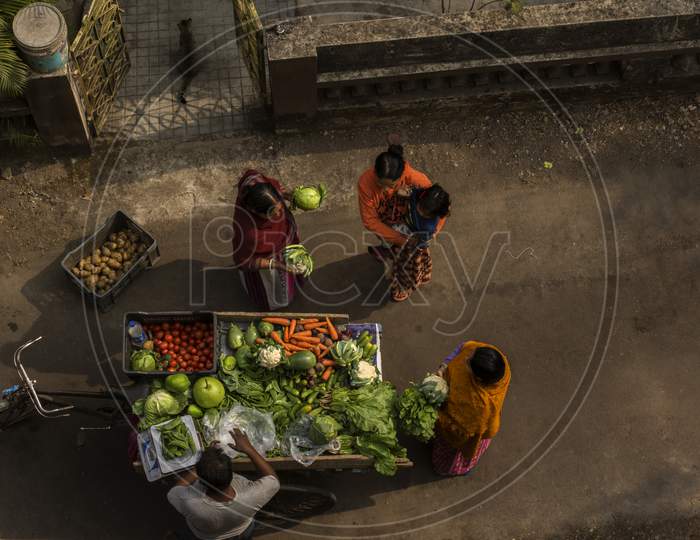 A Vegetable Seller Selling Vegetables Door To Door On His Cycle Van And Three House Wives Buying From Him.
