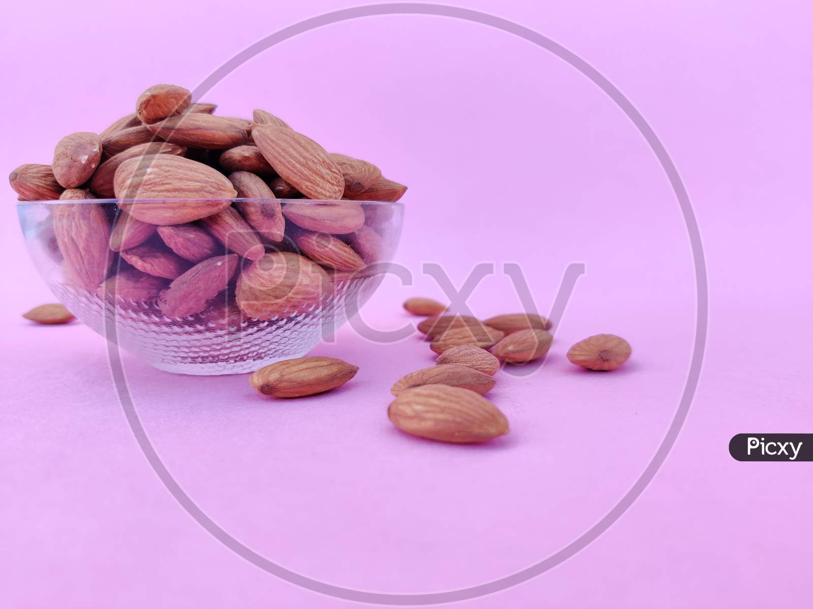 Side View Of A Glass Bowl Full Of Almonds. Pink Background