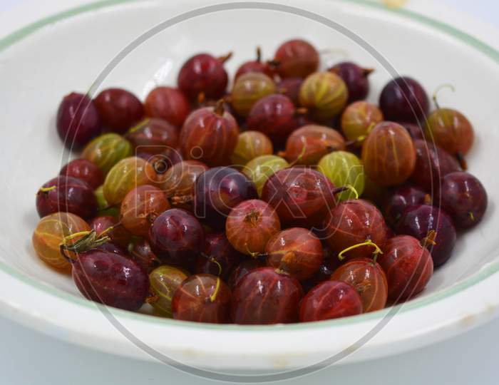 Delicious ripe fruits of red juicy gooseberries arranged in a handful on a white matte background with bright lighting. Useful and healthy food for the human body, delicious sweet and sour fruits.