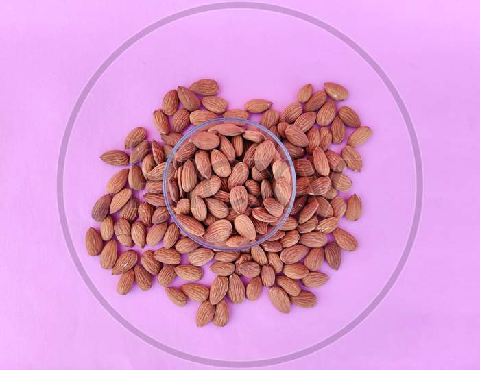 Top View Of A Glass Bowl Filled With Almonds. Pink Background