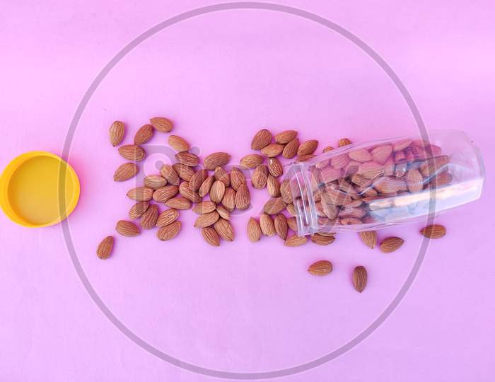Top View Of Pile Of Almonds Pour From Plastic Container. Isolated On Pink Background. Healthy
