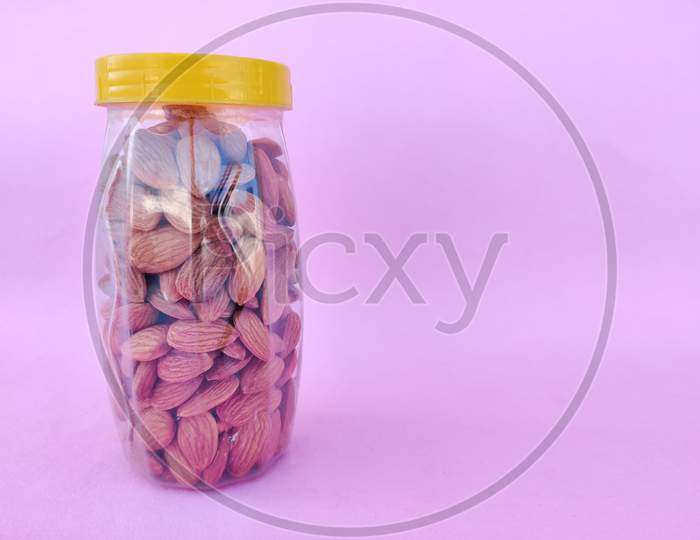 A Plastic Bottle With Yellow Cap Is Filled With Healthy Almonds. Pink Background. Copy Space