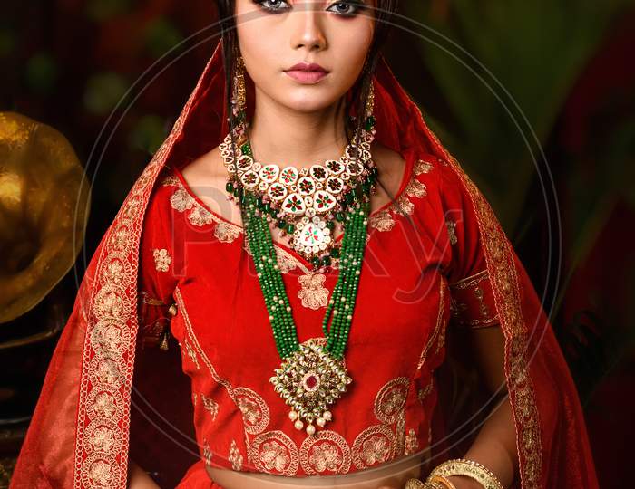 Image of Magnificent Young Indian Bride In Luxurious Bridal Costume With  Makeup And Heavy Jewellery Is Sitting In A Chair In With Classic Vintage  Interior In Studio Lighting. Wedding Fashion.-GC704229-Picxy