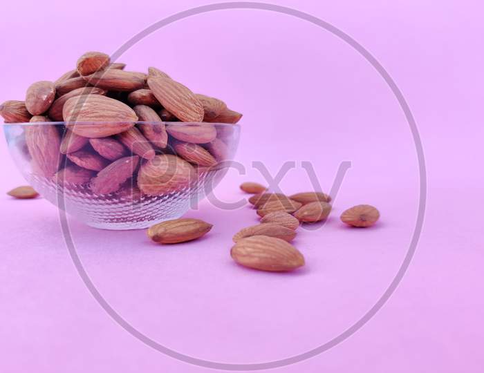 Side View Of A Glass Bowl Full Of Almonds. Pink Background