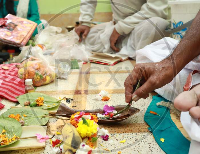 A Hand Performing Hindu Ritual Pooja Yajna Indoor With Flowers And Brass Utensil