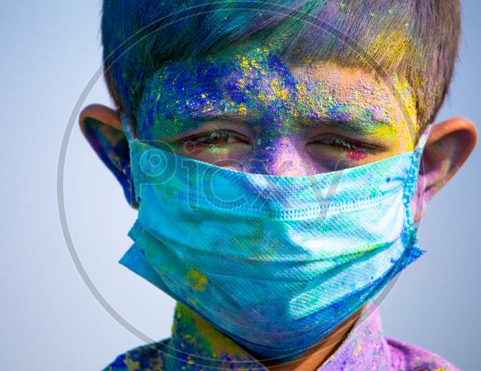 Young Boy With Medical Face Mask Played Holi During Festival Of Colours And Looking Into Camera - Concept Of Holi Celebration During Covid-19 Coronavirus Pandemic.