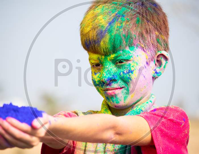 Side View Of Young Smiling Kid With Face Full Of Holi Powder Giving Color To Camera - Concept Of Holi Festival Celebration.