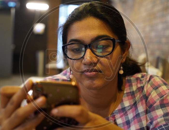 A Young Lady In Spectacles Looking Attentively At Her Phone With Selective Focus On Face