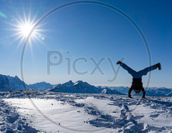 handstand straddle on snow caped mountain peak with blue sky and bright sunbeams.