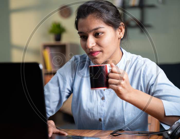 Young Business Woman Having Coffee While Busy Working On Laptop - Concept Of Taking Break, Relaxing Or Enjoying Coffee During Work.