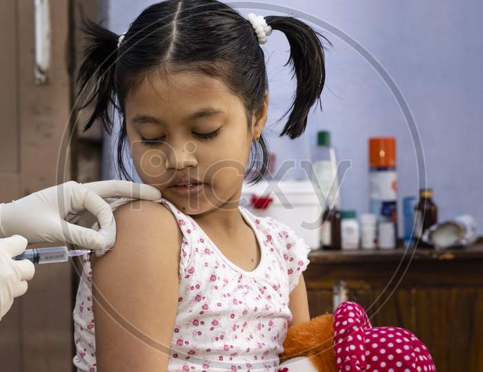 An Indian Girl Child With Doll In Hand Looks On During Vaccination