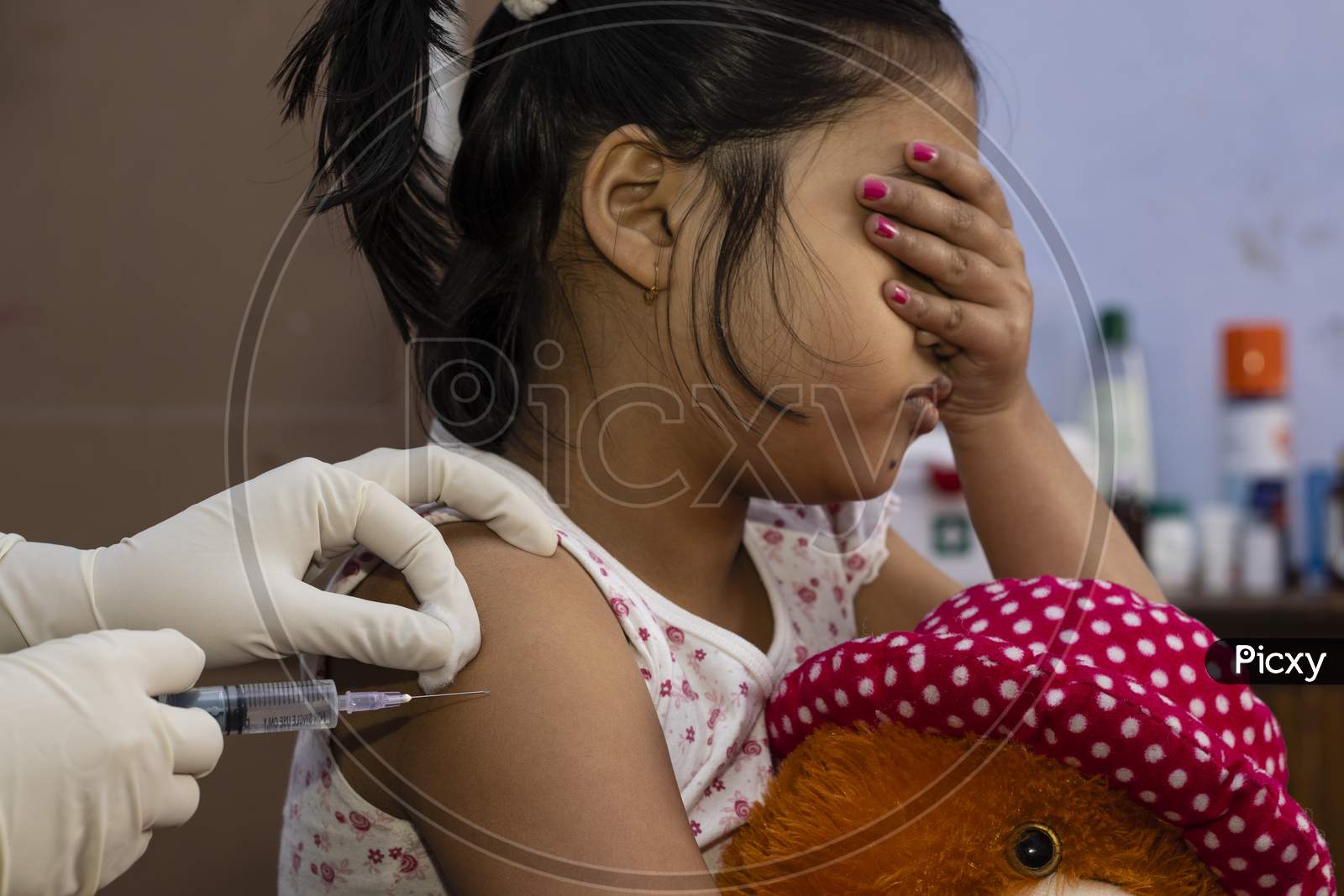 An Indian Girl Child With Doll Covers Her Eyes In Fear During Vaccination
