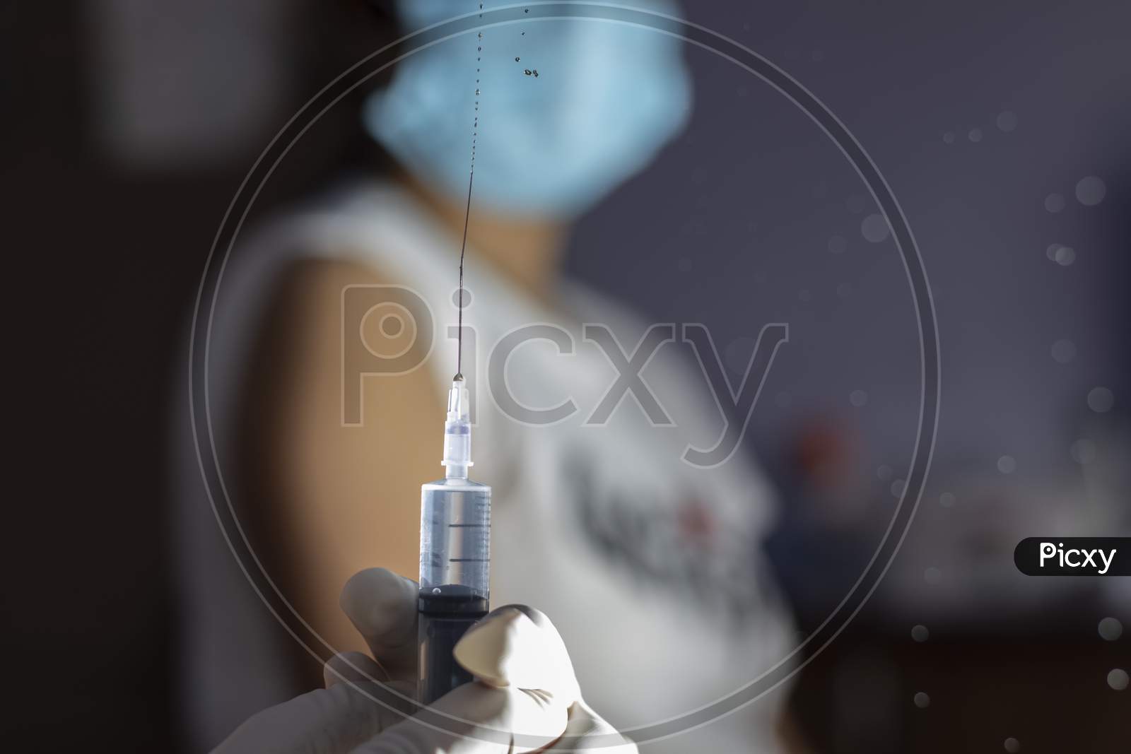 Selective Focus On An Injection Syringe In Hands While A Blurred Woman In Background Looks On